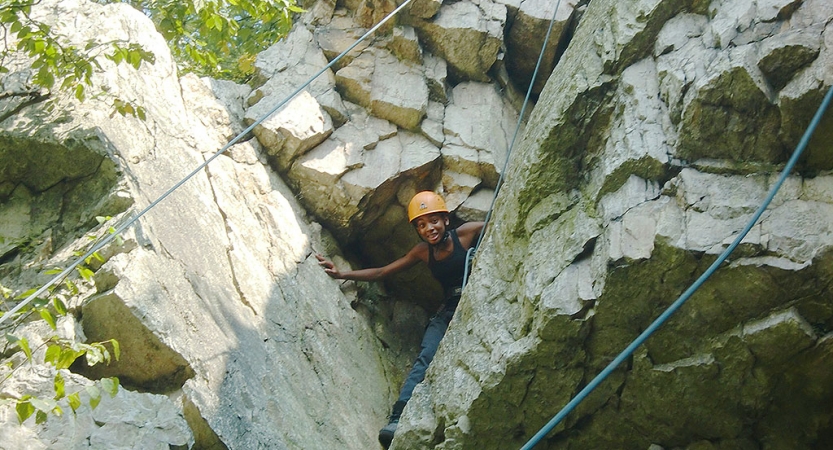 A person wearing safety gear peers out from a rock formation